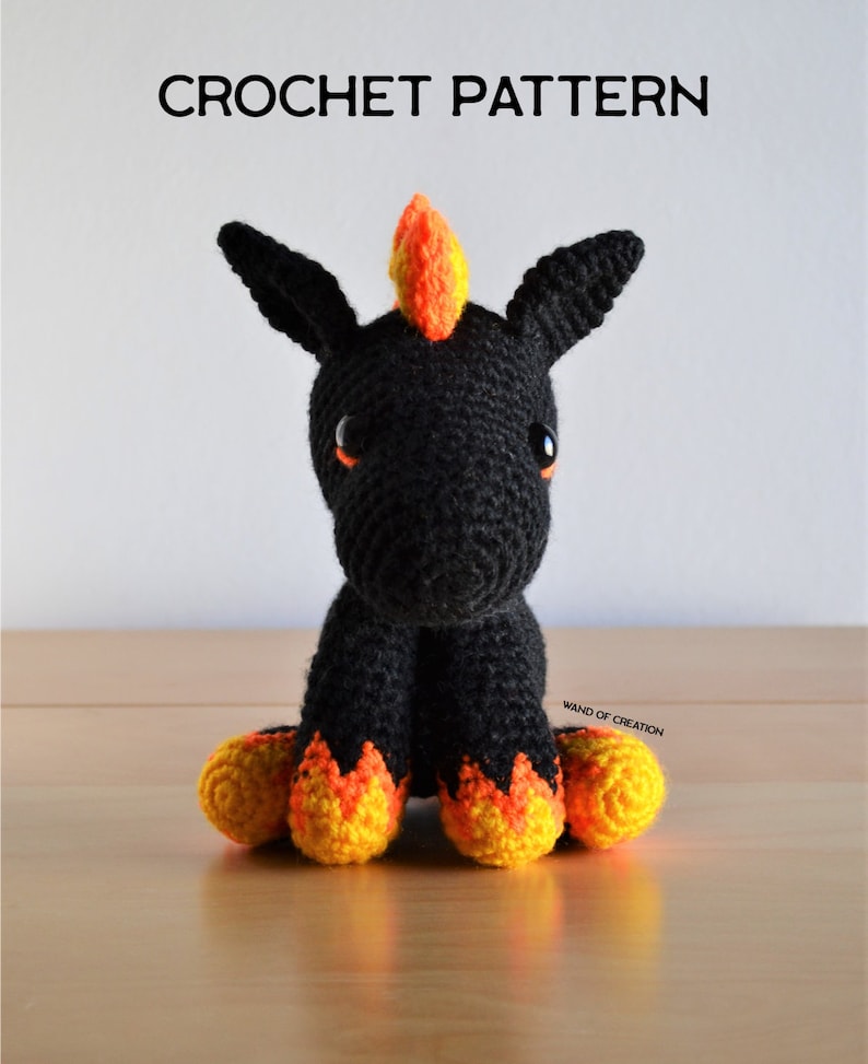 May include: A handcrafted black crochet unicorn with orange and yellow detailing. The unicorn features large, black ears, orange eyes, and a flame-shaped mane. The text "CROCHET PATTERN" is displayed above the unicorn.
