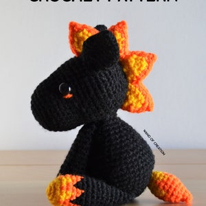 May include: A crocheted dragon toy, predominantly black with orange and yellow detailing. The dragon features a spiky mane and tail. The image includes the text "CROCHET PATTERN" at the top.
