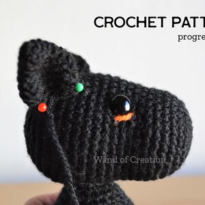 May include: A black crocheted animal head with a large black eye and orange detail, in progress. Red and green pins secure the crochet. The image includes the text "CROCHET PATTERN progress photo" at the top. The item is handmade.