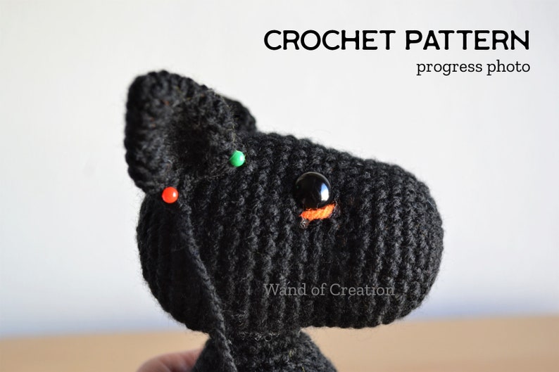 May include: A black crocheted animal head with a large black eye and orange detail, in progress. Red and green pins secure the crochet. The image includes the text "CROCHET PATTERN progress photo" at the top. The item is handmade.