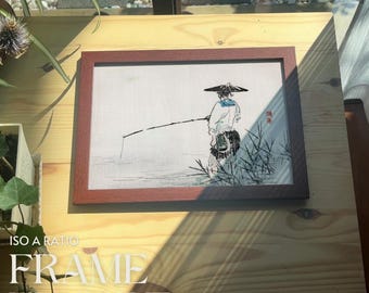 May include: A framed black and white ink drawing of a person fishing in a river. The drawing is on a light brown background and is framed in a dark brown frame. The frame is on a light brown wooden surface.