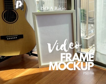 May include: A white picture frame with a wood-like finish sits on a wooden floor. The frame is empty and has a white mat. The text "Video Frame Mockup" is written in white on the floor in front of the frame. The text "PSD File" is written in white below the frame.