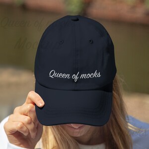 Puede incluir: Gorra de b&eacute;isbol azul marino con la inscripci&oacute;n "Queen of mocks" bordada en blanco. La gorra tiene un dise&ntilde;o cl&aacute;sico de seis paneles, una visera curva y una correa ajustable.