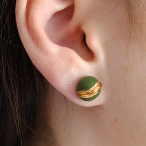 Peut inclure: Une paire de boucles d'oreilles clous vertes et dorées. Les boucles d'oreilles sont rondes et ont un accent doré.
