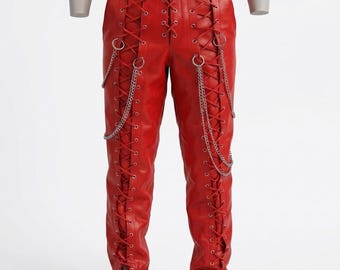May include: Red leather pants with a lace-up design on the front and sides. Silver-colored chains hang from the waist and sides. The pants have a fitted silhouette and are displayed on a mannequin.