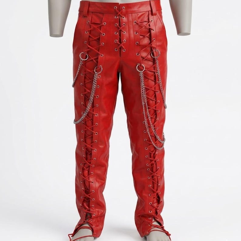May include: Bright red leather trousers featuring a lace-up design on the front and sides. Silver chains hang from the waist and sides. The trousers have a fitted shape and are displayed on a mannequin.