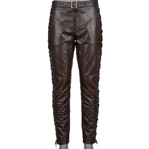 May include: Brown leather pants with a lace-up front and sides. The pants have a belt with a gold buckle. The leather appears to be distressed, giving the pants a vintage look. The pants are designed with multiple panels and stitching.