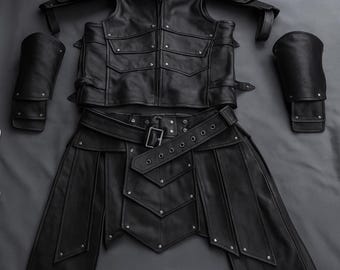 Può includere: Un set di armature in pelle nera, composto da un gilet con tasche, spalline, protezioni per le braccia e una gonna con cintura. L'armatura è rifinita con rivetti e fibbie ed è disposta su una superficie scura.