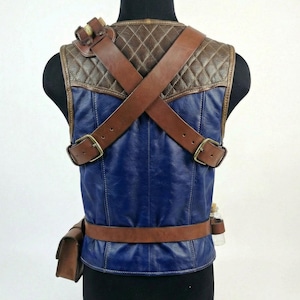 May include: A blue and brown leather vest with brown straps and buckles. The vest has a quilted brown shoulder section and a brown belt with a small pouch. A small glass bottle is attached to the side.