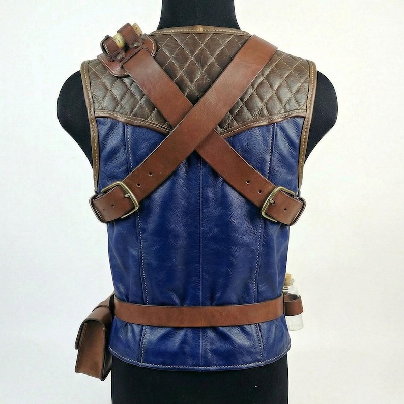 May include: A blue and brown leather vest with brown straps and buckles. The vest has a quilted brown shoulder section and a brown belt with a small pouch. A small glass bottle is attached to the side.