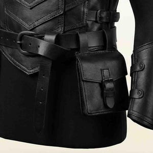 Puede incluir: Una prenda de cuero negro con un corpi&ntilde;o estructurado con costuras en chevron, un cintur&oacute;n ancho con hebilla met&aacute;lica y una bolsa rectangular adjunta con solapa de hebilla. Un protector de brazo de cuero a juego es visible a la derecha.