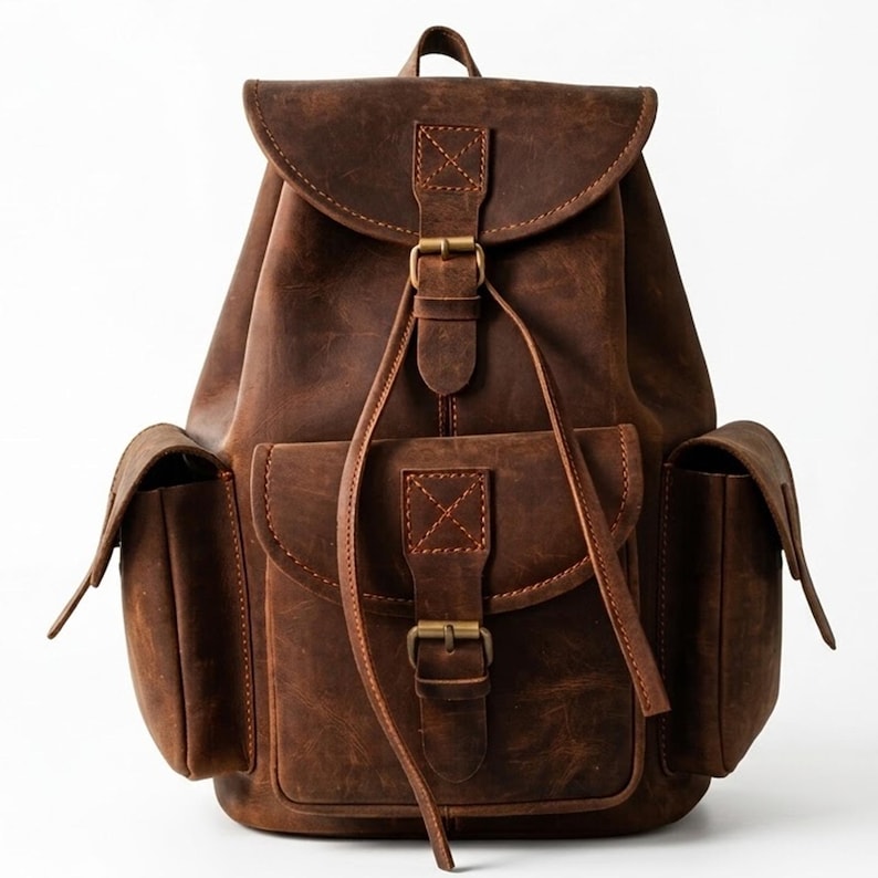 May include: A dark brown leather backpack featuring a large main compartment with a flap closure, a front pocket, and two side pockets. Each pocket and the main flap are secured with brass-toned metal buckles and leather straps with stitching.