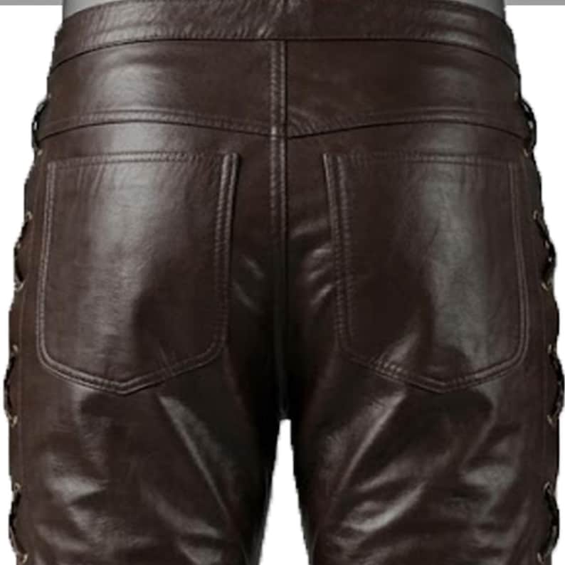 May include: Close-up of brown leather pants with two back pockets and decorative lacing on the sides. The leather has a glossy finish and visible stitching details. The pants appear to be well-tailored.