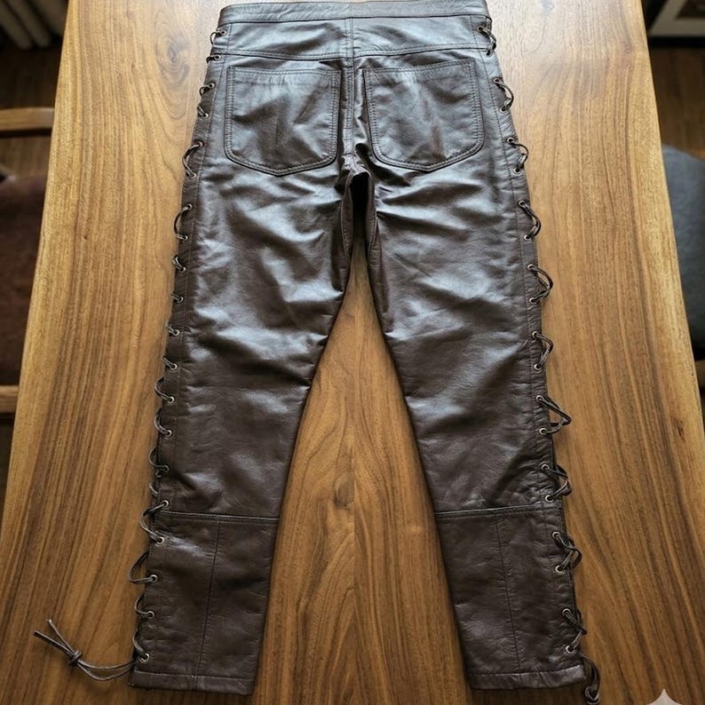 May include: Brown leather pants with lace-up detailing along the sides. The pants have two back pockets and a classic five-pocket design. The leather has a slightly distressed appearance.