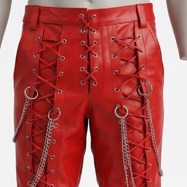 May include: Red leather trousers featuring a lace-up design. Silver chains and rings are attached to the lace-up details. The trousers have a classic five-pocket design and a belt loop.