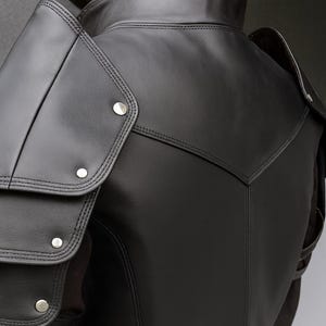 以下が含まれることがあります： シルバーリベット付きの黒革ショルダーアーマー。アーマーは、重ねられたショルダーパッドと詳細なステッチが特徴です。アーマーの背面はV字型デザインです。