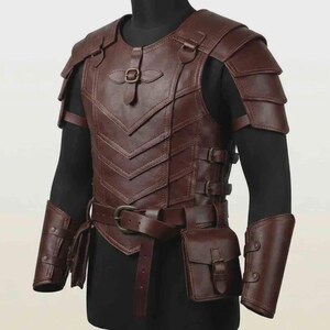 Puede incluir: Una pieza de armadura de pecho de cuero marr&oacute;n oscuro con hombreras superpuestas, una hebilla central en el pecho y un cintur&oacute;n con una bolsa adjunta. La armadura incluye brazaletes a juego y se asegura con m&uacute;ltiples hebillas laterales.