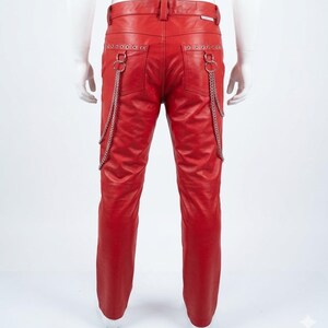 May include: Red leather trousers with silver chain detailing hanging from the back pockets. The trousers have a classic five-pocket design and a straight leg cut. The trousers are shown on a mannequin.