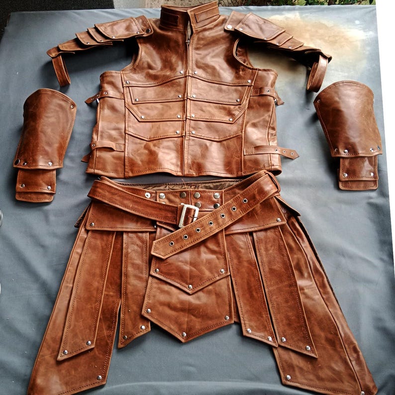K&ouml;nnte beinhalten: Ein braunes Leder-R&uuml;stungsset, bestehend aus einer Weste mit Taschen, Schulterpolstern, Armsch&uuml;tzern und einem Rock mit G&uuml;rtel. Die R&uuml;stung ist mit Nieten und Schnallen versehen, was auf ein mittelalterliches oder Fantasy-Thema hindeutet.