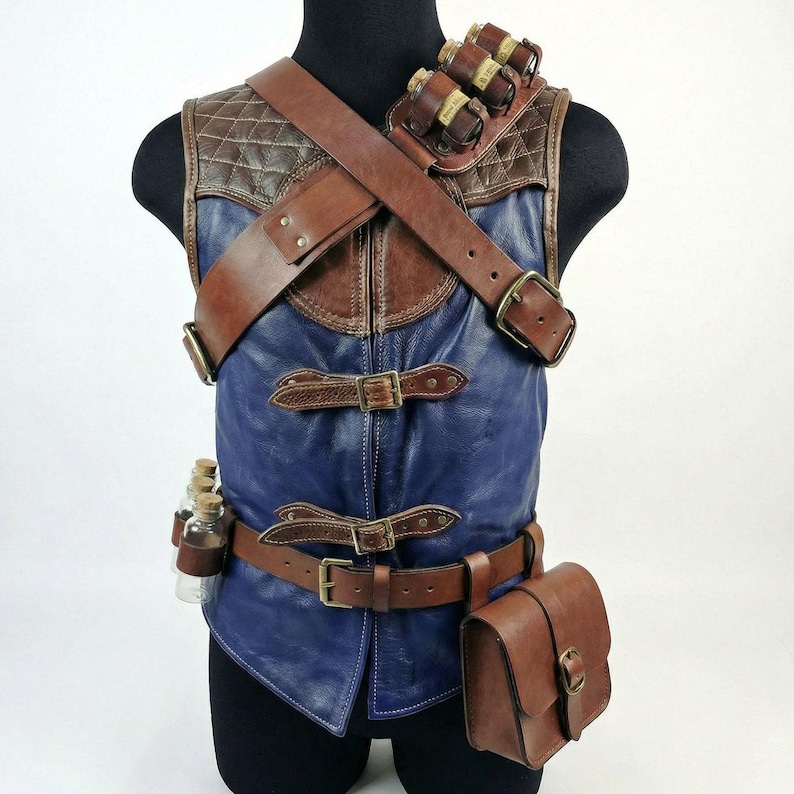 May include: A handcrafted leather vest in brown and blue, featuring multiple straps, buckles, and pouches. The vest has a quilted brown leather shoulder piece and a blue leather body. Small glass bottles are attached to the vest, along with a brown leather satchel.