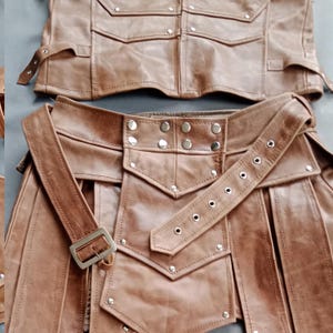 K&ouml;nnte beinhalten: Zweiteiliges Outfit aus braunem Leder. Das Oberteil hat mehrere Taschen und Riemen. Das Unterteil hat einen G&uuml;rtel mit Schnalle und dekorativen Nieten. Das Outfit scheint handgefertigt zu sein und hat eine robuste, Vintage-&Auml;sthetik.