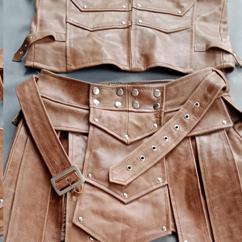K&ouml;nnte beinhalten: Zweiteiliges Outfit aus braunem Leder. Das Oberteil hat mehrere Taschen und Riemen. Das Unterteil hat einen G&uuml;rtel mit Schnalle und dekorativen Nieten. Das Outfit scheint handgefertigt zu sein und hat eine robuste, Vintage-&Auml;sthetik.
