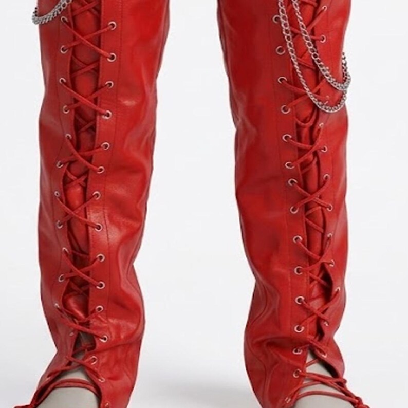 May include: Vibrant red knee-high boots featuring a lace-up design and silver chain detailing. The boots have a smooth, leather-like finish and a pointed toe. Red laces crisscross up the front of the boots.