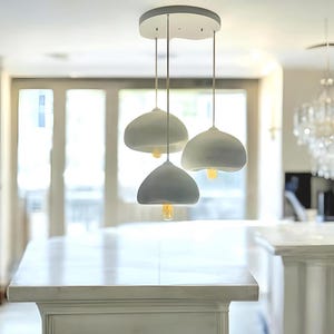 Pode incluir: Um candeeiro pendente branco com tr&ecirc;s c&uacute;pulas redondas, brancas e em forma de cogumelo. O candeeiro est&aacute; pendurado num acess&oacute;rio de teto branco.