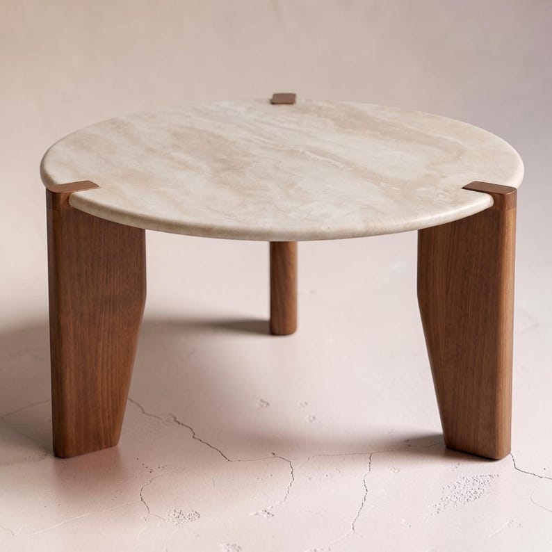 May include: A round coffee table featuring a smooth, beige, veined stone top surface supported by three thick, dark brown wooden legs that extend upward to meet the edge of the stone, creating a sturdy and balanced furniture piece.