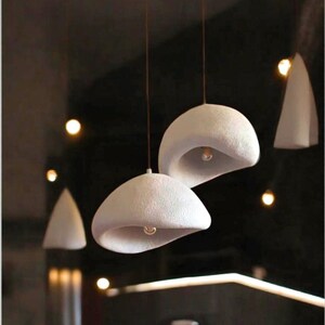 Pode incluir: Tr&ecirc;s luzes pendentes de cer&acirc;mica branca com acabamento texturizado. As luzes t&ecirc;m a forma de uma c&uacute;pula arredondada com um furo no centro. As luzes est&atilde;o penduradas no teto.