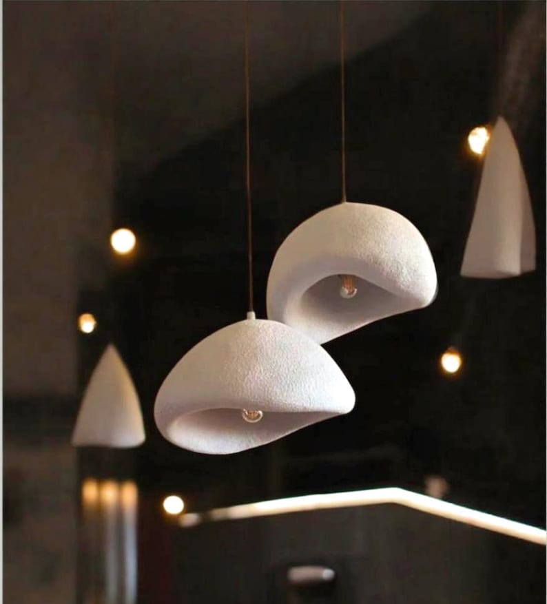 Pode incluir: Tr&ecirc;s luzes pendentes de cer&acirc;mica branca com acabamento texturizado. As luzes t&ecirc;m a forma de uma c&uacute;pula arredondada com um furo no centro. As luzes est&atilde;o penduradas no teto.