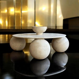 May include: A white marble coffee table with an oval top and three round legs. The table is sitting on a black surface.