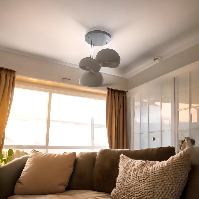 Pode incluir: Uma sala de estar com um sof&aacute; marrom e almofadas bege. Uma lumin&aacute;ria de teto branca com tr&ecirc;s abajures redondos pendurados acima do sof&aacute;.