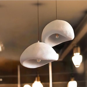 Pode incluir: Dois pendentes de cer&acirc;mica branca texturizada com um formato org&acirc;nico &uacute;nico. As luzes est&atilde;o penduradas no teto e t&ecirc;m l&acirc;mpadas expostas.