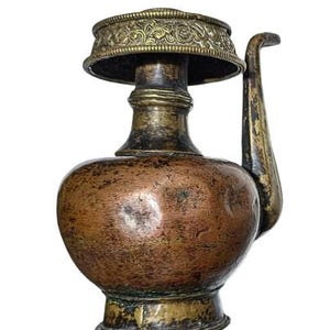 May include: An antique copper and brass pitcher with a bulbous body and a decorative, ornate rim. The pitcher has a curved spout and a handle. The metal has a weathered, aged appearance, with variations in color from bronze to gold.
