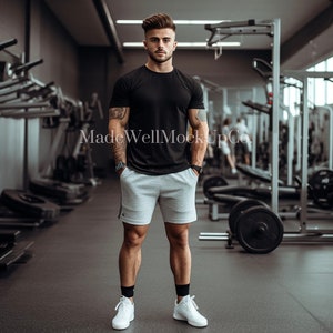 May include: A man wearing a black t-shirt and gray athletic shorts stands in a gym. He is looking at the camera. The gym has weightlifting equipment in the background.
