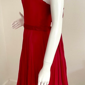 May include: A sleeveless, fuchsia pink dress with a gathered skirt and a fitted bodice. The dress has a sheer overlay at the neckline and a satin sash at the waist.