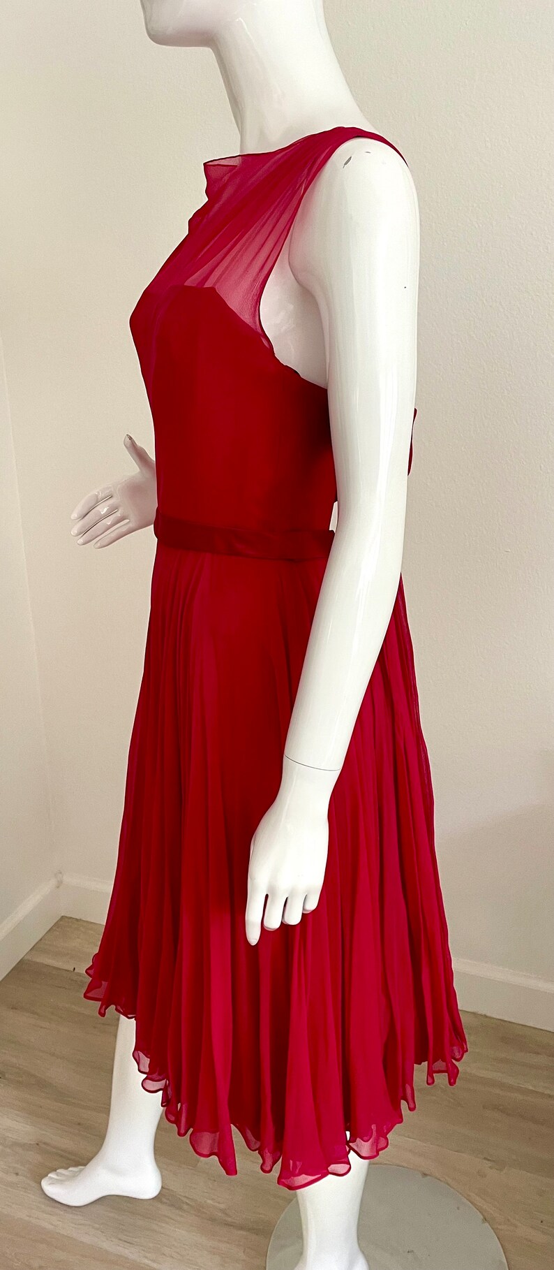 May include: A sleeveless, fuchsia pink dress with a gathered skirt and a fitted bodice. The dress has a sheer overlay at the neckline and a satin sash at the waist.