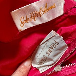 May include: A pink silk dress with a white label that says "Saks Fifth Avenue" and a white label that says "Frank Starr" with the size "7/8" written on it.