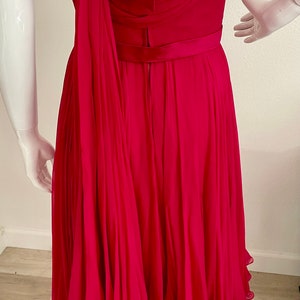 May include: A fuchsia pink dress with a pleated skirt and a bow at the back. The dress has a sleeveless design and a fitted bodice.