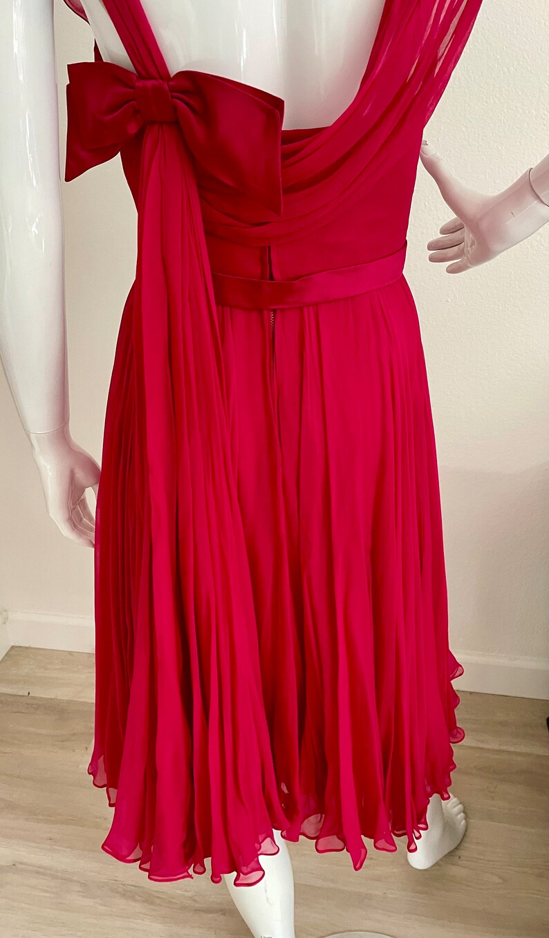 May include: A fuchsia pink dress with a pleated skirt and a bow at the back. The dress has a sleeveless design and a fitted bodice.