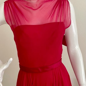 May include: A sleeveless, fuchsia-coloured dress with a sheer, ruffled neckline and a fitted bodice. The dress has a wide, satin belt and a flowing skirt.