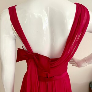 May include: A fuchsia pink sleeveless gown with a large bow at the back. The gown has a fitted bodice and a flowing skirt.