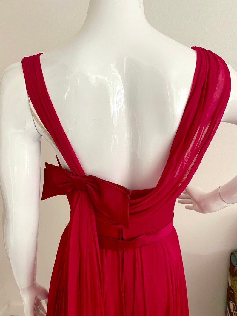 May include: A fuchsia pink sleeveless gown with a large bow at the back. The gown has a fitted bodice and a flowing skirt.