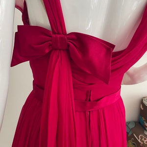 May include: A crimson red dress with a large satin bow at the back. The dress has a fitted bodice and a flowing skirt.