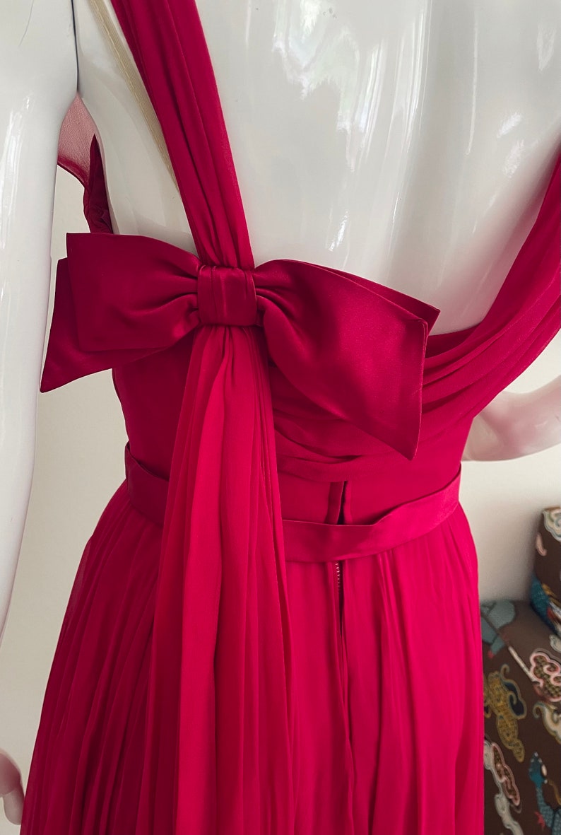 May include: A crimson red dress with a large satin bow at the back. The dress has a fitted bodice and a flowing skirt.
