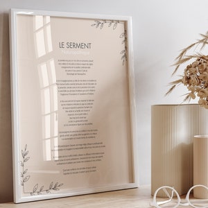 Puede incluir: Una impresión enmarcada en blanco con el texto "LE SERMENT" y un poema francés sobre el juramento hipocrático. La impresión está sobre una mesa de madera con dos cajones blancos, un par de gafas redondas blancas y dos jarrones beige con hierba de la pampa seca.