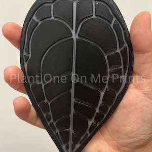 May include: A black 3D printed leaf with a detailed vein pattern. The leaf is shaped like a heart and has a textured surface.