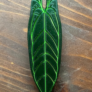 May include: A 3D printed green leaf with a detailed vein pattern. The leaf is shaped like a heart and has a light green outline.