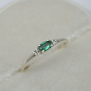 Puede incluir: Un anillo de plata con una esmeralda ovalada verde y pequeños diamantes transparentes en la banda.